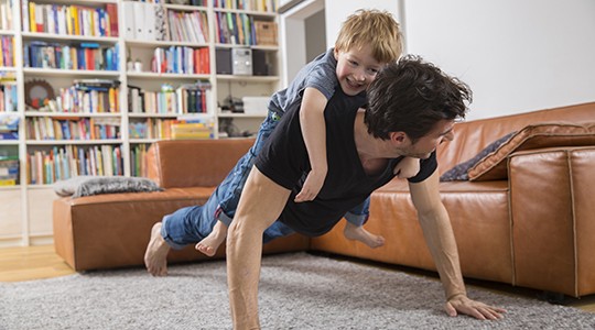 man doing push ups with his son on laughing on his back in the living room 