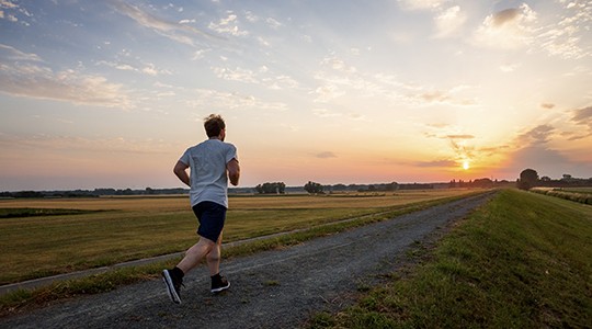 man running down a dirt road among a flat landscape into the sunset