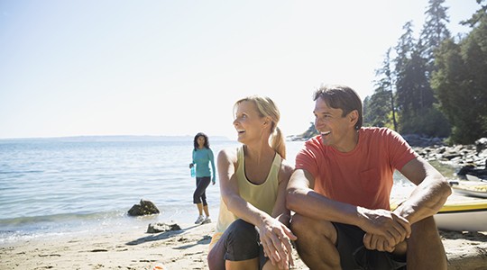 man and woman on the beach in activewear smiling and looking out at the water with a woman in the background