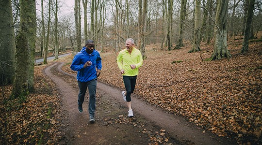 two older men jogging a dirt path in the woods during fall